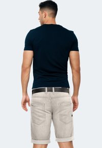 Marineblaues Baumwoll-T-Shirt mit kurzen Ärmeln, kombiniert mit hellgrauen Jeansshorts mit umgeschlagenen Säumen und hinteren Taschen. Schwarzer Ledergürtel inklusive.