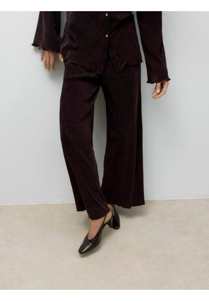 Ensemble de loungewear en velours côtelé marron foncé comprenant un pantalon à jambes larges et un haut à bouton avec des poignets effilochés, le tout associé à des talons aiguilles noirs.