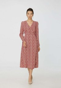 Robe florale rouge avec des manches longues, un décolleté en V et une longueur midi fluide. Présente des motifs de feuilles blanches et une taille cintrée.