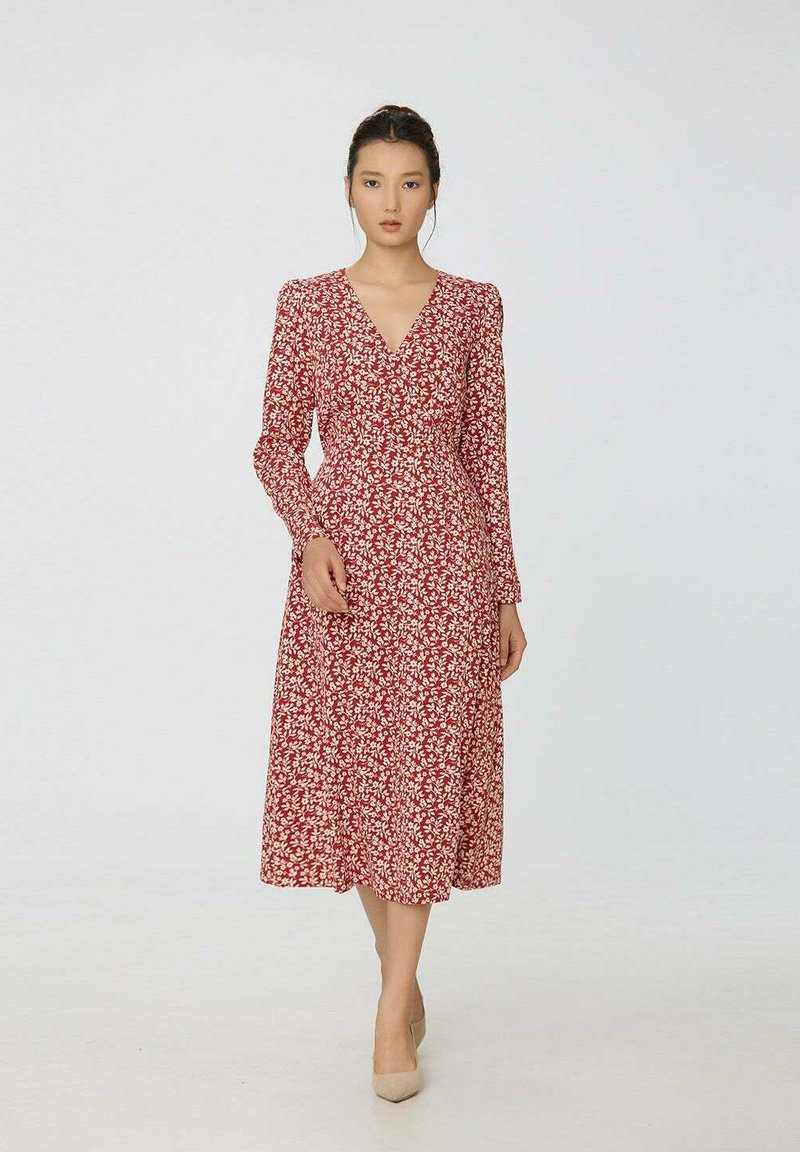 Robe florale rouge avec des manches longues, un décolleté en V et une longueur midi fluide. Présente des motifs de feuilles blanches et une taille cintrée.