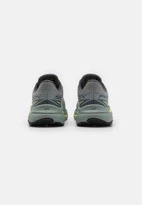 Gray athletic shoes with a textured upper, yellow accents, and a cushioned sole, featuring branding and a supportive heel design.