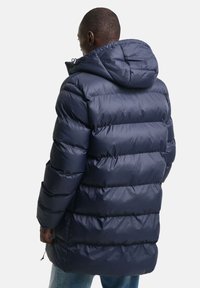 Marineblå pufferjakke med hætte, prydet med en quiltet design, elastiske manchetter og en snoretræk i kanten for justerbar pasform.