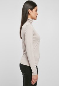 Lichtbeige coltrui, getailleerd ontwerp, lange mouwen, zachte textuur, gladde stof, gecombineerd met donkere jeans, minimalistische styling.
