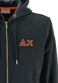 Felpa con zip nera, con ricamo di un triangolo arancione e una X sul petto, rifiniture arancioni della zip e delle coulisse con punte metalliche.