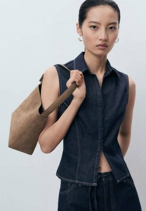 Haut sans manches en denim foncé avec un design ajusté, des boutons sur le devant et des coutures contrastantes. Assorti à un sac à épaule en daim taupe.