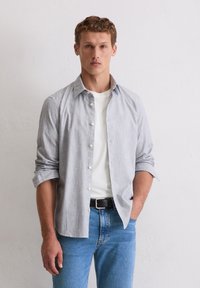 Koszula na guziki w jasnoszare paski, rękawy podwinięte, noszona na białym t-shircie. Dopełnieniem stroju są niebieskie dżinsy i czarny pasek.