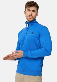 Blå fleece-pullover med høj krave, halv lynlås lukning og broderet logo. Den har ribbede manchetter og lige søm.