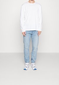 Camisa blanca de manga larga, jeans azul claros y zapatillas blancas con detalles azules. Ajuste casual con un diseño simple y sin patrones.