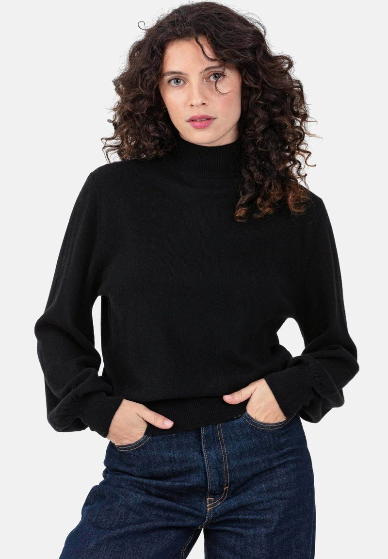 Pull à col roulé noir avec poignets et ourlet côtelés, fabriqué en tissu doux et texturé. Associé à un jean bleu.
