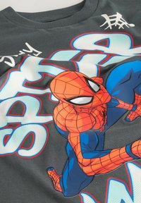 Pelēka T-kreklu ar lielu krāsainu Spider-Man grafiku, kurā ir spilgti oranžie un zili toņi, kā arī baltas teksta akcenti.
