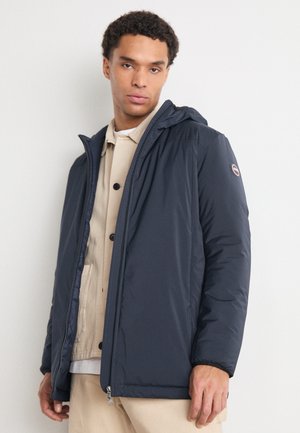 Giacca puffer blu navy con cappuccio, dotata di zip frontale e chiusura a bottoni, insieme a un badge con logo sulla manica. Tessuto liscio e isolato.