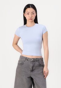 T-shirt cropped de manga curta azul claro com decote redondo, feito de um tecido suave. Combinado com calças de ganga cinza de cintura alta.