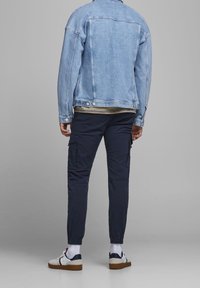 Ljusblå denimjacka med framfickor, lagd över en beige topp. Mörk marinblå cargobyxor med fickor och elastiska muddar. Vita sneakers med detaljer.