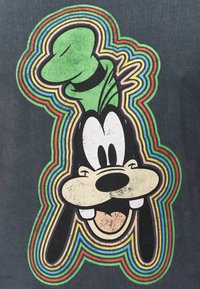 Maglietta nera con una grande stampa grafica di un personaggio dei cartoni animati con un cappello verde. Il design è contornato da cerchi concentrici colorati.