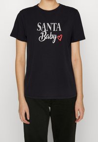 Musta puuvillapaita, jossa on teksti "SANTA Baby" valkoisena ja punaisena, pyöreä kaula-aukko, lyhyet hihat ja normaali istuvuus.
