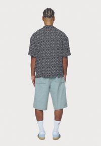 Kortärmad svart och vit mönstrad skjorta sedd bakifrån, i kombination med ljusblå denimshorts och vita strumpor med blå detaljer.