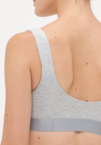 Woman's upper back and shoulder wearing a light gray sports bra with wide straps and elastic band, against a plain white background.