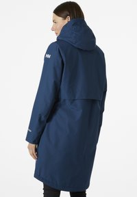 Marine regenjas gemaakt van waterdicht materiaal, voorzien van een capuchon, lange mouwen en reflecterende accenten. Volledige lengte met ventilatie aan de achterkant.