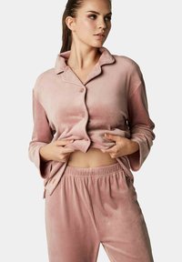 Roze, zachte velours loungewear set met een knoopsluiting shirt met een gesneden kraag en elastische tailleband broek. Soepele textuur, relaxed fit.