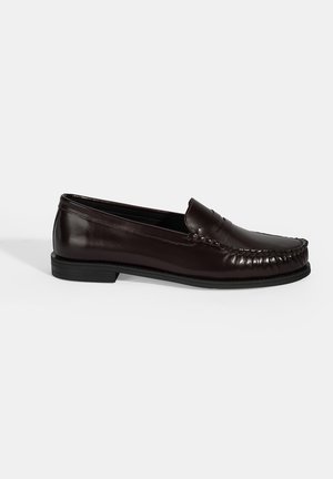 Bruine leren loafers met een gladde afwerking, voorzien van decoratieve stiksel langs de bovenkant en een platte zwarte rubberen zool.
