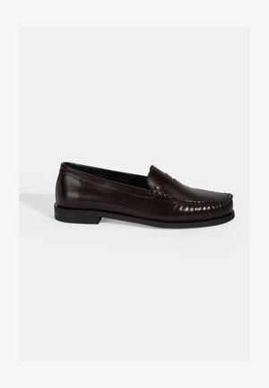 Braune Lederloafers mit einer glatten Oberfläche, die dekorative Nähte entlang des Oberteils und eine flache schwarze Gummisohle aufweisen.