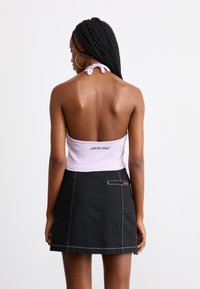 Top corto halter di colore viola chiaro con dettagli di chiusura sul retro, abbinato a una mini gonna nera con cuciture bianche e una tasca laterale.
