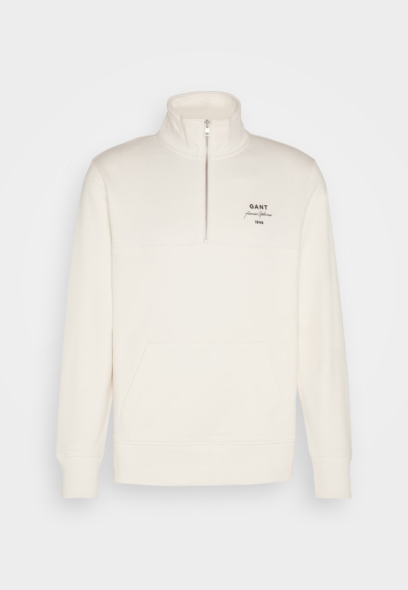 Felpa cremosa con zip e colletto alto, tasca frontale e logo del marchio ricamato in nero. Tessuto morbido con polsini e orlo a coste.