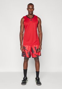 Röd idrottstanktop med svart kant; röda shorts med ett svart abstrakt mönster; svarta strumpor och sportiga skor med gröna accenter.