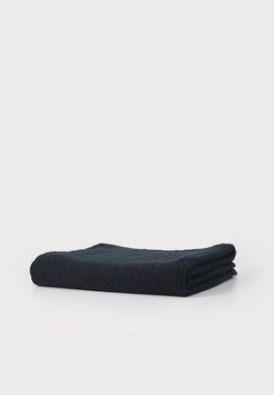 Cobertor de algodão texturizado, de cor azul escuro, dobrado com cuidado. Apresenta um padrão acolchoado subtil. Macio e espesso, com bordas bem acabadas.