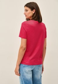 Upnuté, krátké tričko s krátkým rukávem v jasně růžovém bavlněném provedení; hladká textura; kulatý výstřih; kombinované se světle modrými džíny.