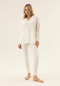 Biała bluzka z długim rękawem w kształcie litery V o luźnym kroju, zestawiona z białymi legginsami z prążkowanego materiału. Miękka tkanina, gładka faktura i minimalistyczny design.