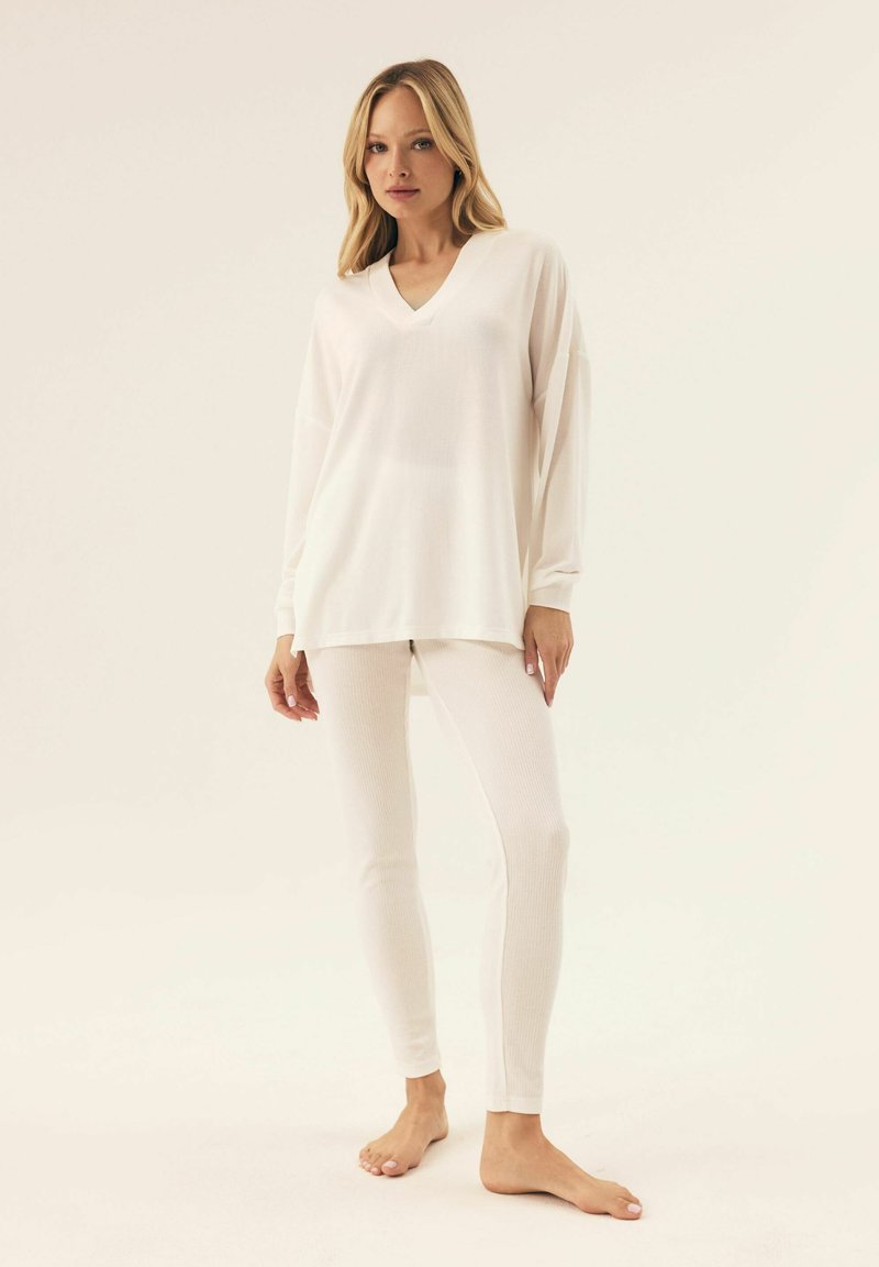 Biała bluzka z długim rękawem w kształcie litery V o luźnym kroju, zestawiona z białymi legginsami z prążkowanego materiału. Miękka tkanina, gładka faktura i minimalistyczny design.
