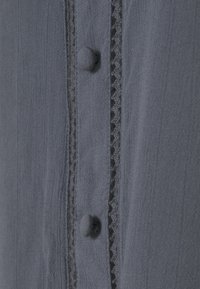 Grått tyg med små knappar och en strukturerad remsa med vågiga kanter samt vertikala linjer. Slät och lätt textur.