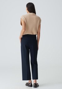 Beige ribbad stickad topp med korta ärmar, kombinerad med marinblå raka byxor med elastisk midja och bakfickor. Bruna skor.