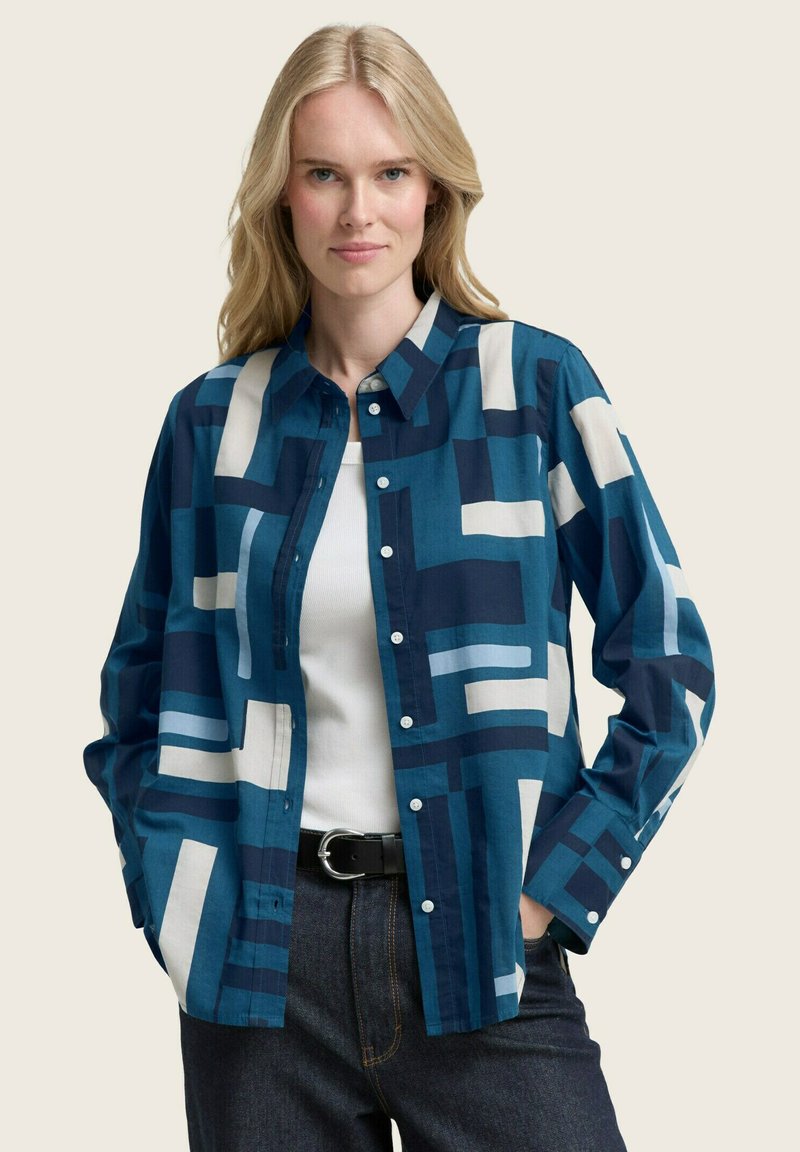 Camicia button-up con motivi geometrici blu e beige, realizzata in cotone, con colletto e maniche lunghe. Tessuto morbido, vestibilità rilassata.