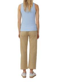 Lichtblauw geribbeld tanktop, beige wijde broek met rafelige zomen en witte sneakers met lichtblauwe accenten. Gezien vanaf de achterkant.