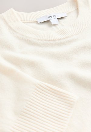 Kremowy sweter dziergany z prążkowanym kołnierzem i wykończeniami na rękawach. Wykonany z miękkiego materiału, z subtelną teksturą na całej powierzchni.