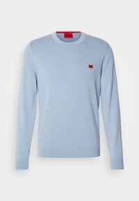 Pull bleu clair à manches longues avec col rond, poignets et ourlet côtelés, arborant un petit logo de marque rectangulaire rouge sur la poitrine.