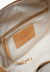 Tan leren interieur met een gouden rits, stofvoering en een gemerkte tan leren tag. Beschikt over een haak voor sleutels of accessoires.