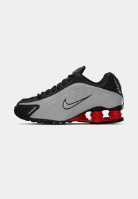 Sapatilha Nike preta e cinza com almofadas de calcanhar em formato de mola vermelhas e logo Swoosh preto na lateral, vista lateral em fundo branco.