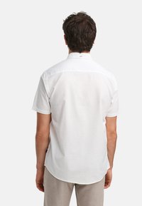 Camisa blanca de manga corta hecha de algodón, con un dobladillo curvado y un cuello clásico, notable por una etiqueta cerca del cuello para la marca.
