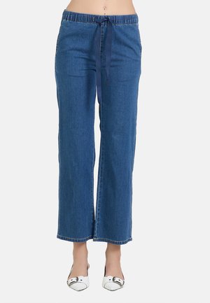 Pantaloni di denim blu a vita alta con elastico in vita e coulisse blu navy, indossati con scarpe bianche con punta appuntita.
