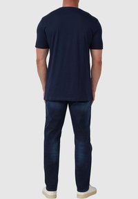 Marineblauwe katoenen T-shirt met een ronde hals, korte mouwen en een rechte pasvorm, gecombineerd met donkere spijkerbroeken en witte sneakers.