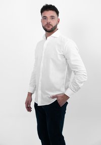 Witte linnen overhemmed met een standaardkraag, lange mouwen en een rechte zoom, gecombineerd met donkere broeken. Gladde textuur, minimale details.