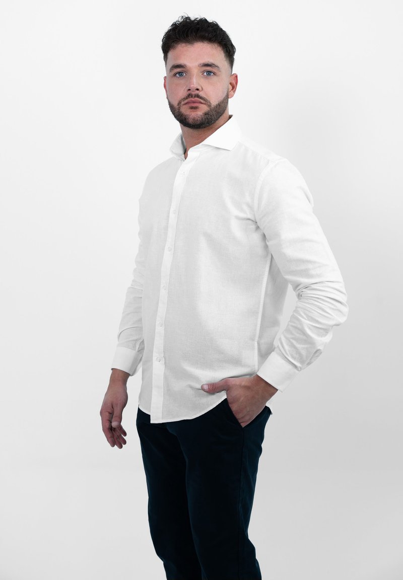 Witte linnen overhemmed met een standaardkraag, lange mouwen en een rechte zoom, gecombineerd met donkere broeken. Gladde textuur, minimale details.
