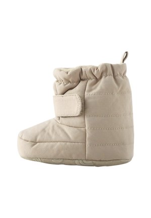 Bottine bébé beige matelassée avec une bride velcro, une semelle souple, une cheville froncée et une languette à l’arrière pour un enfilage facile.