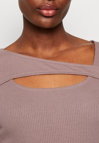 Ribbat, mauvafärgad topp med asymmetrisk utskärning vid halsringningen och breda axelband. Mjuk textur, figursydd form.