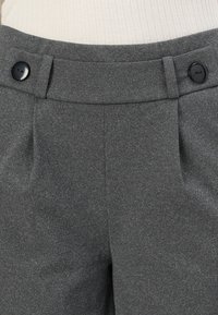 Pantalon gris taille haute avec large ceinture, deux passants pour ceinture et boutons noirs de chaque côté de la ceinture.
