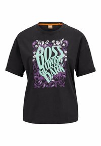 Černé tričko s krátkým rukávem a ohrnutými manžetami, na kterém je tyrkysovým písmem nápis "BOSS GLOWING IN THE DARK" nad fialovým květinovým a listovým grafickým designem.