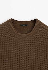 Brun strikket sweater med ribbet rund halsudskæring. Har et struktureret mønster og blødt stof. Mærket er synligt indeni kraven.